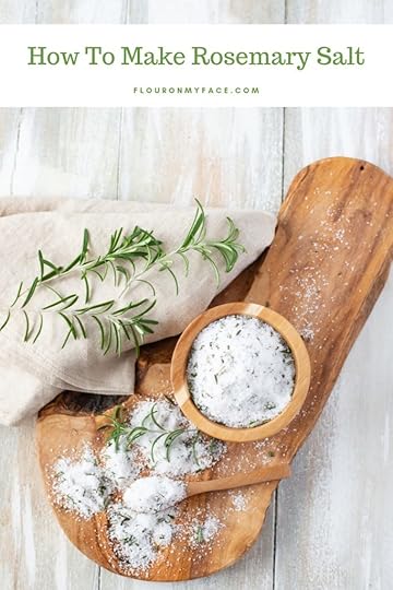Homemade Rosemary Salt on a wooden cutting board with a fresh rosemary sprig and a tan linen napkin.