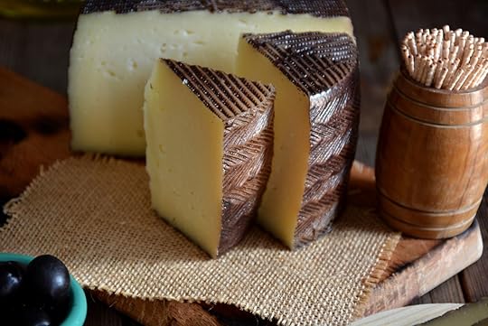 Pieces of manchego cheese cured on a wooden table accompanied by olives