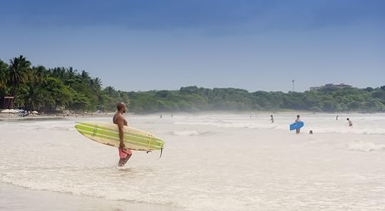 Young man walking with his surfboard into sea in Tamarindo, Costa Rica