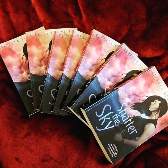 Seven glorious ARCs of Shatter the Sky , fanned out over a red fabric background.