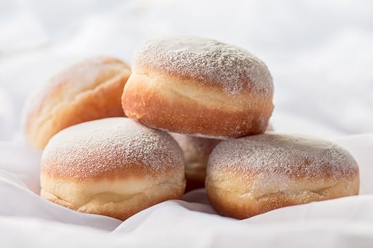 Jelly filled donuts with powdered sugar on a bed with white sheets