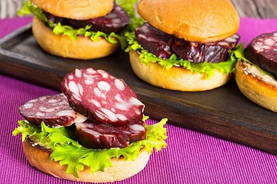 delicious sandwiches with butter, lettuce and slices of smoked sausage in fried bun on dark wooden board on table mat