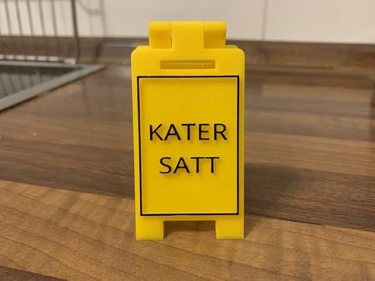 Ein gelber Aufsteller, auf dem in schwarzer Schrift und schwarzem Rahmen „Kater satt“ steht.
