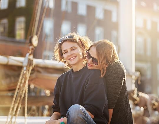 Two happy young women are sitting side by side embracing on the street, Copenhagen, Denmark