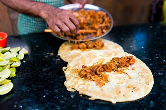 Two chicken and egg kathi rolls with onions being prepared on a blackboard with green limes by a street food vendor in Kolkata
