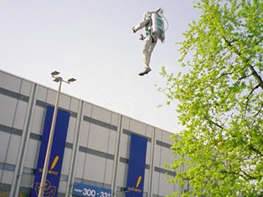Man in Rocketpack flying in front of blue and white building.