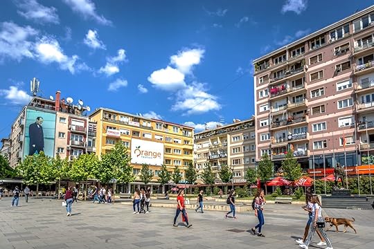 Big group of people walking in front of colorful buildings in a blue skies day in Kosovo