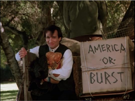 Balki is riding on the back of a horse-drawn cart. The cart is filled with straw, a caged chicken, and an 