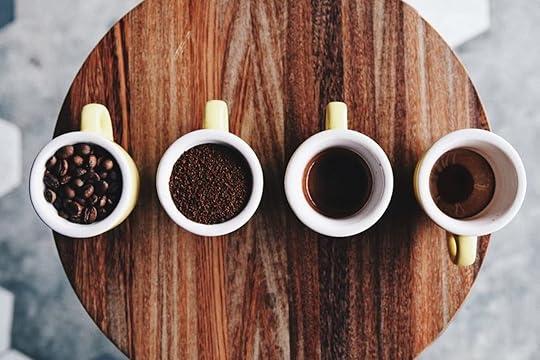 Four cups of coffee, grounds, and beans lined up on a wood table