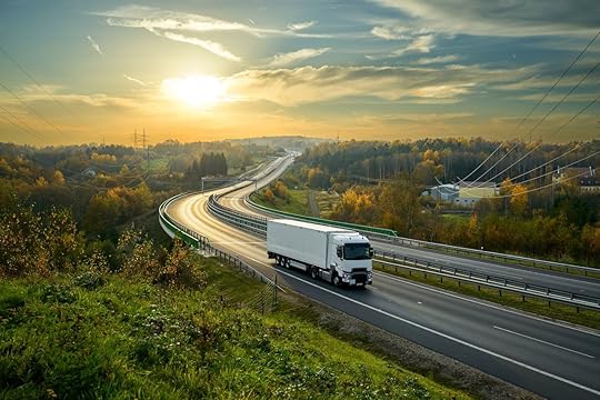 White truck driving on the highway winding through forested landscape in autumn colors at sunset