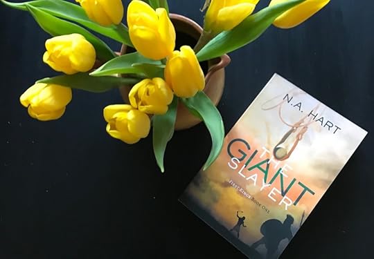 A bouquet of yellow tulips and the book The Giant Slayer on a black table.