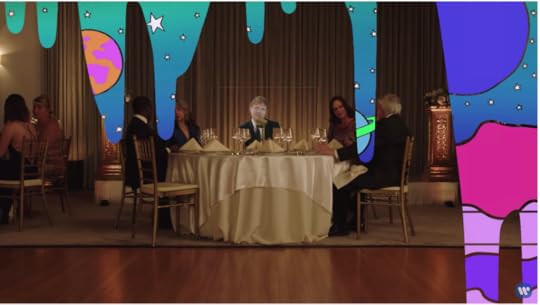Ed, still horribly green screened, is sitting at a table in the fancy restaurant, but now there are drips of a second background cascading down, revealing brightly colored planets and stars that look like a kid drew them in art class.
