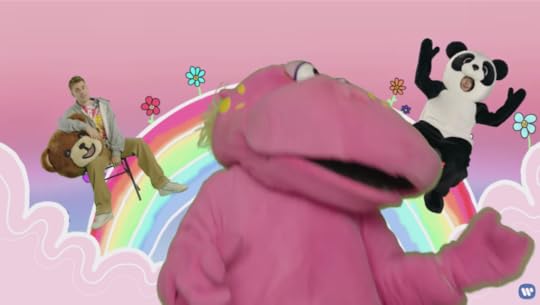Justin, in totally normal street clothes, is sitting in a folding chair on an animated rainbow while holding the bear suit head in his lap. Miserable Panda Ed is on the other side of the rainbow. The pink hippo dances in the foreground