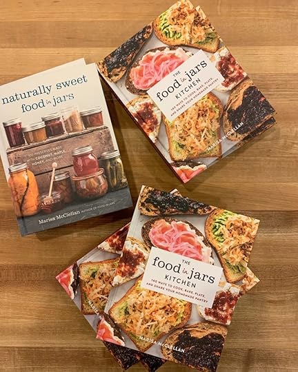 Stacks of Naturally Sweet Food in Jars and The Food in Jars Kitchen on a wooden table. Both are cookbooks by Marisa McClellan.