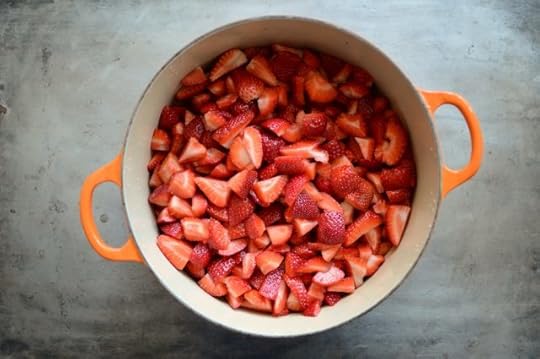 An orange Le Creuset pot with quartered strawberries on a metal surface.