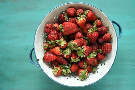 Strawberries in a blue and white colander on a painted green board.