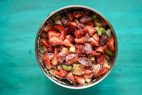 Chopped strawberries and rhubarb mixed with sugar in a stainless steel bowl on a painted green board.