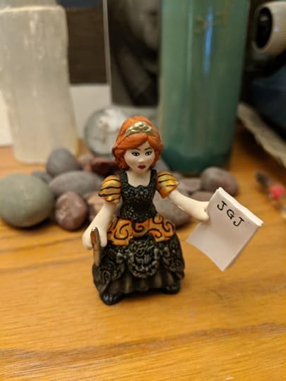 A small princess figure with red hair and a notepad with JGJ written across the top and a pen in her other hand.