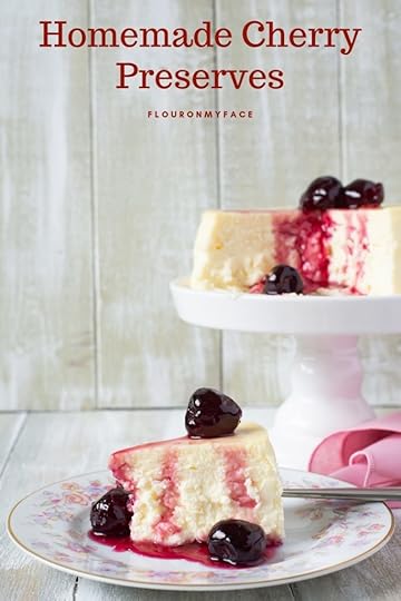 A slice of cheesecake on a vintage dessert plate with a serving of homemade Cherry Preserves with a cake stand in the background with the cheesecake topped with no pectin homemade cherry preserves with a pink cloth napkin on the tables.