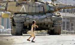 A screenshot from the film Occupation of the American Mind showing a Palestinian boy throwing a rock at an Israeli tank.