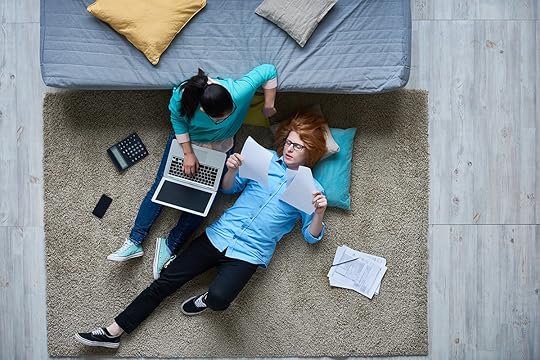 Two people look at bills on a bedroom floor