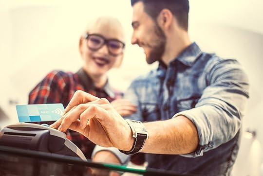 A man goes to swipe his credit card. He is shown smiling and standing next to a woman who is also smiling