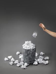 Hand throwing crumpled paper into a bin
