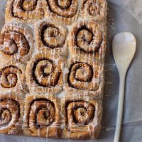 dozen cinnamon rolls on parchment paper with glazing