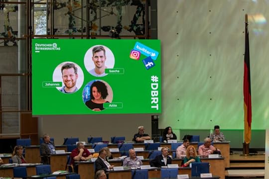 Ein großer Bildschirmen mit drei Köpfen des Social-Media-Teams, einer davon meiner.