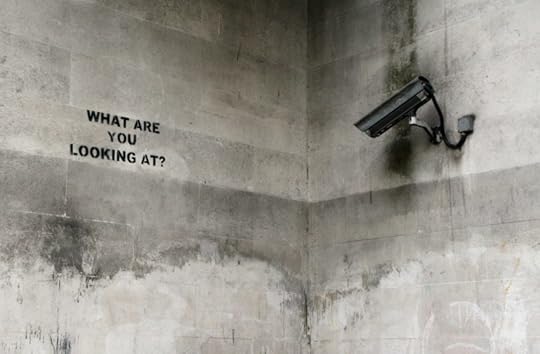 A CCTV camera points to a wall with a spraypainted 'what are you looking at?' written on it.