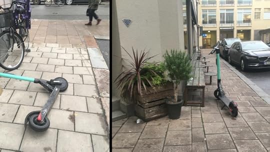 Two electric scooters, one lying down across the sidewalk and one parked on the sidewalk.