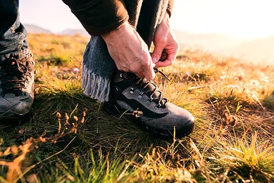 close-up of person tying walking boot. Outdoors, scarf, grass.