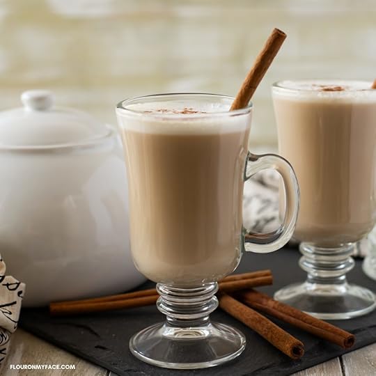 A mug of Crock Pot Chai Latte topped with frothy milk. cinnamon and garnished with a cinnamon stick. A white tea pot is in the background