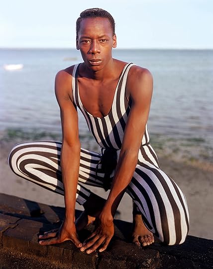 subject wearing striped bodysuit crouching on the sand in front of the ocean