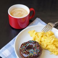 coffee with plate of scrambled eggs and chocolate donut