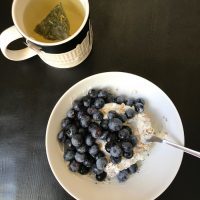 bowl of yogurt and muesli and berries with a mug of green tea
