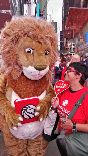 Leonard in a lion outfit and Sumana in street clothes, facing each other among the crowds of Times Square.