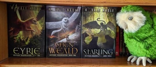 A book shelf with the hardcover editions of Eyrie, Ashen Weald, and Starling face-out to show off the covers. To the right is a stuffed animal ground parrot.