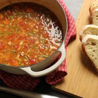 pot of tomato based soup with slices of bread on cutting board