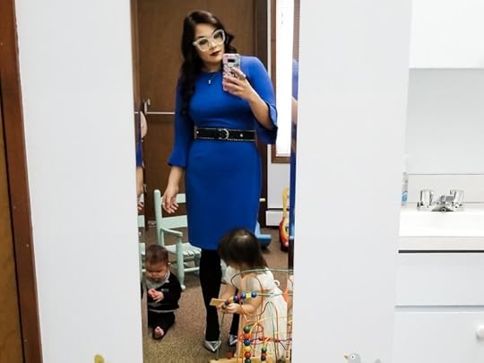 A mother takes a fashion selfie in front of a mirror in a children's playroom while two children play.