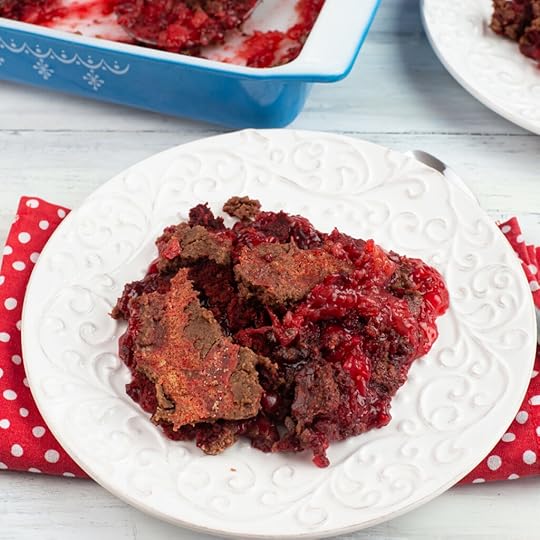 photo of a serving of red velvet dump cake on a white plate with a red and white polka dot cloth napkin with the baking pan in the background