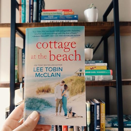 Cottage at the Beach by Lee Tobin McClain in a woman's hand in front of a bookshelf