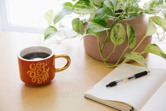 red mug sitting on desk with plant and journal