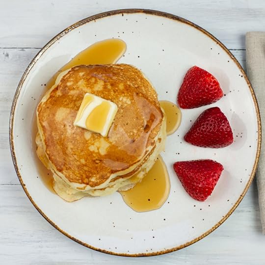 Sourdough Pancakes with a pat of butter drizzled with syrup a plate with sliced strawberries