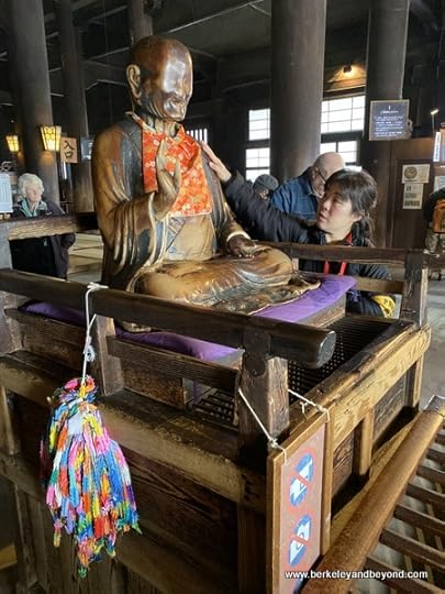woman places hand on shoulder of Obinzuru-sama at Zenkoji Temple in Nagano City, Japan