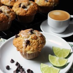 chocolate chip muffin on plate on table next to cooling rack with espresso