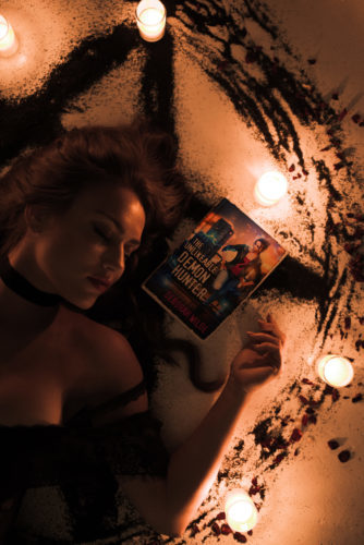 Woman laying in lit up circle with The Unlikable Demon Hunter book by Deborah Wilde.