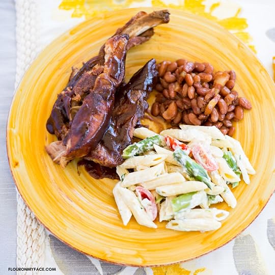 Smoky BBQ Spare ribs served with a side of baked beans and a pasta salad on a yellow glass plate.