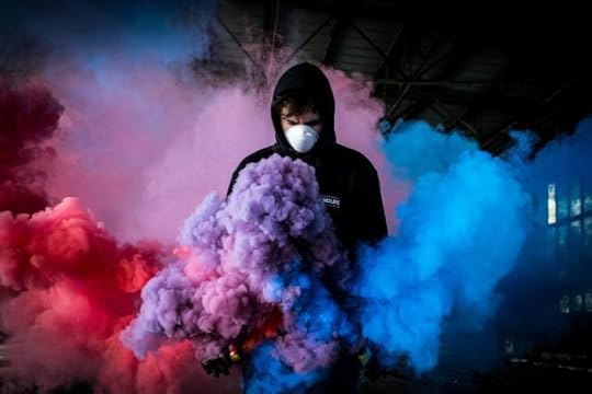 treated - a figure in a hoodie and mask moving through clouds of colorful smoke.
