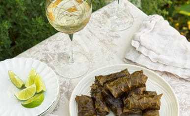 Grape leaf tamales on a plate with some white wine and limes.